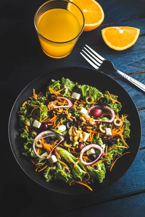 A tall glass jar of the Sunrise Green Smoothie made with organic spinach, mango, and pineapple, garnished with a mango slice and fresh mint sprig on a wooden surface